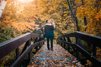 Man carrying his fiancée over a bridge with fall leaves covering it