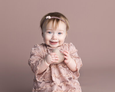 Baby girl sits and smiles for her first year photo session in Wexford,pa with a soft heart in hand.