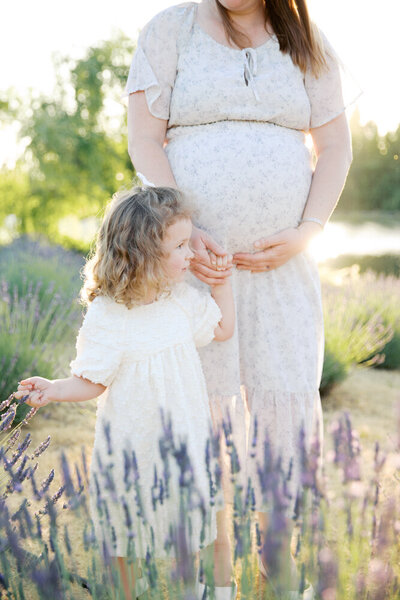 Expecting mother holding hand of big sister standing in the lavender field taken by sacramento family photographer Kelsey Krall