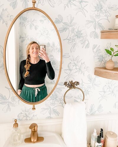 A female diyer taking a selfie in a swivel mirror in her newly renovated powder bathroom.