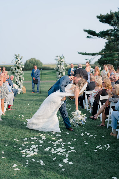 A couple does a dip and kiss as they walk up the aisle after their wedding ceremony