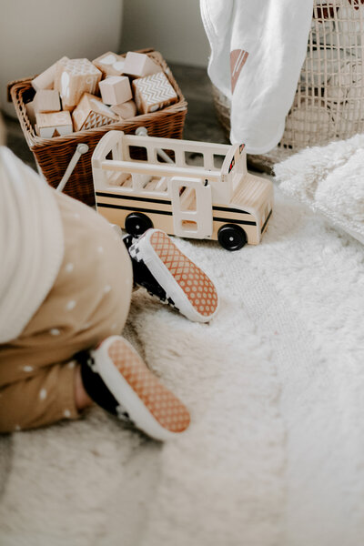 Child in beige polka dot pants sitting on a soft white rug next to a wooden toy bus and a basket of wooden blocks - Family Autism Support Coach at Chantal Hewitt Coaching