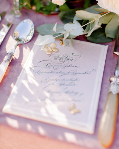 Elegantly calligraphed menu card with gold butterfly details, and a plum tablecloth, photographed by New England Wedding Photographer Ashley Helen