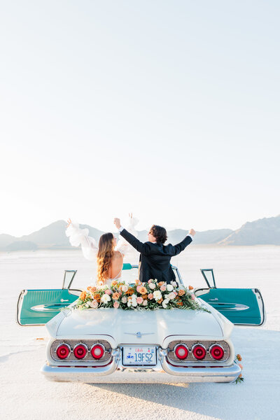a wedding couple sitting on their convertible car on the utah salt flats
