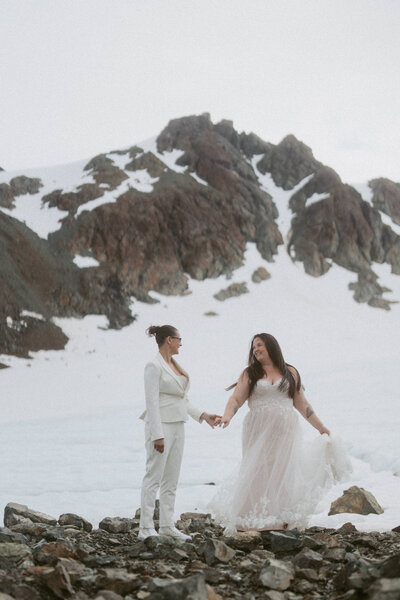 A pair of brides holding hands on a glacier during their elopement in Seward, Alaska.