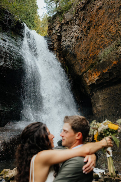 bride and groom hugging with a waterfall in the background
