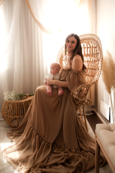 A mother in a gorgeous Reclamation gown holding her baby in a peacock chair.