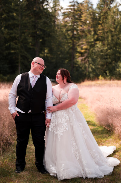 Bride and groom hold hands and walk through field at their country wedding in Edmonton, Alberta