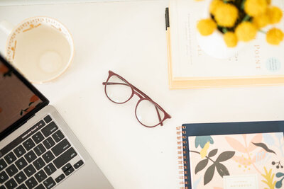 The desk of an email marketing copywriter and strategist features a laptop, cup of coffee, and glasses