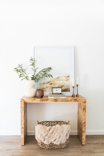 Console Table with brass candles, olive tree branches, basket and blanket, photo, and clock in Encinitas, California.