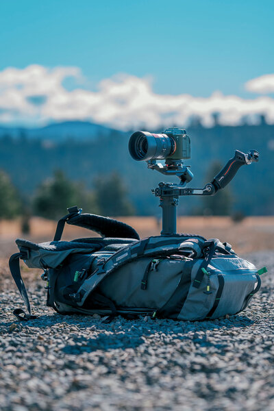 Outdoor setup featuring a camera gimbal sitting on a backpack, part of Joseph Mayden’s stabilized video gear for capturing smooth cinematic footage in remote locations.