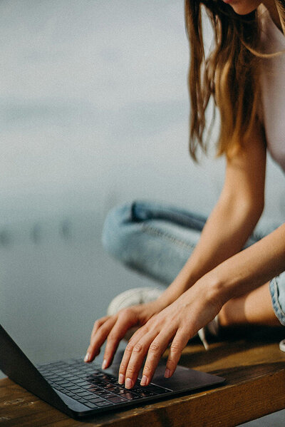 A woman sits on a wooden bench, focused on her laptop, enjoying a moment of productivity outdoors.