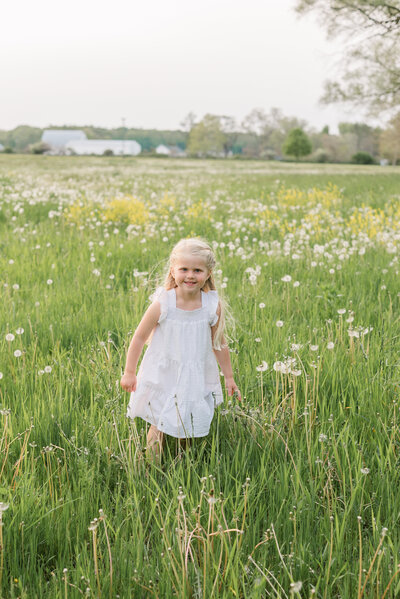 Little girl standing in a flower field surrounded by small white blooms and tall grass.
