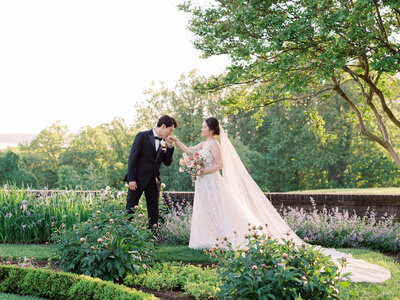 Groom kissing bride’s hand in garden wedding portrait