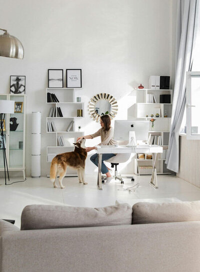 Minimalist home scene that shows a woman petting her dog, surrounded by bookshelves with home decor