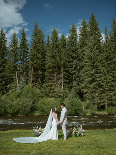 A couple saying their vows in front of a river and tall pines for their Colorado elopement