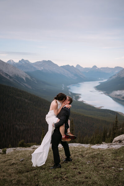 groom holds bride up around his waist as she kisses him during sunrise hiking elopement in kananaskis