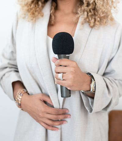 Female speaker wearing neutral blazer holding a microphone in front of her chest.