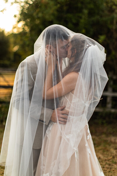 bride and groom kissing under a veil at sunset