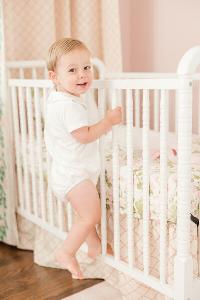 Toddler smiling over his shoulder while climbing into crib.