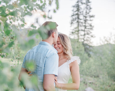 A happy couple snuggles in the trees of Frisco Peak in a white dress and blue shirt