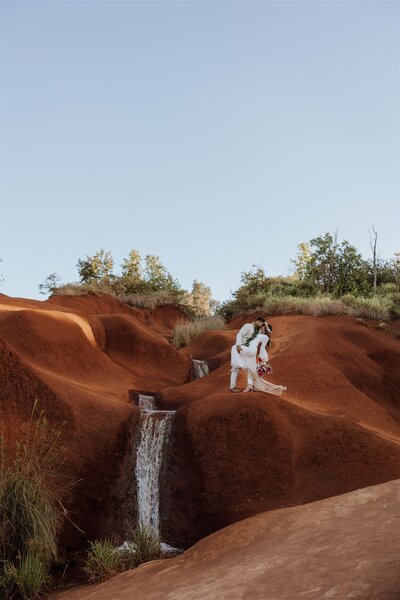groom dipping bride on top of a red dirt waterfall