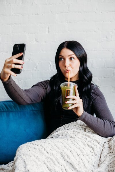 Female model taking a selfie with green Biggby Coffee drink.