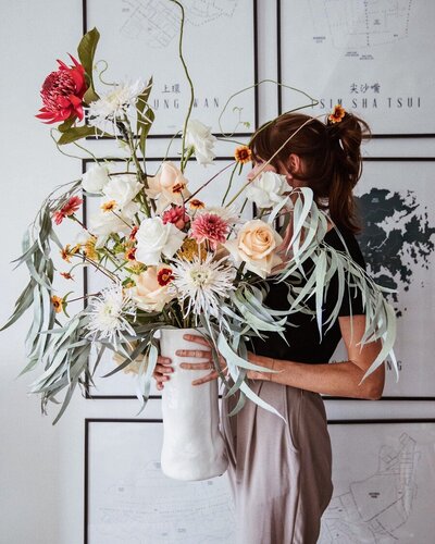 Woman holding large flower bouquet of assorted flowers in front of maps