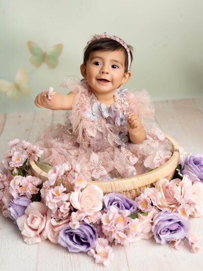 A sleeping baby dressed in a cozy pink outfit and bonnet rests in a nest adorned with green leaves and pink flowers, conveying serenity and warmth.