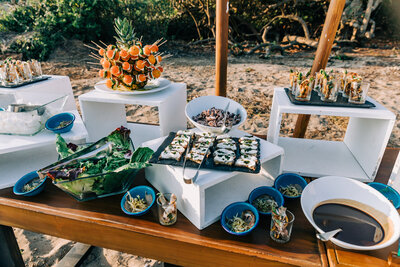 A beautifully arranged wedding reception table featuring an assortment of gourmet appetizers. Set outdoors with natural textures and soft lighting, this setup reflects the attention to detail and elevated experience offered through luxury destination wedding planning.
