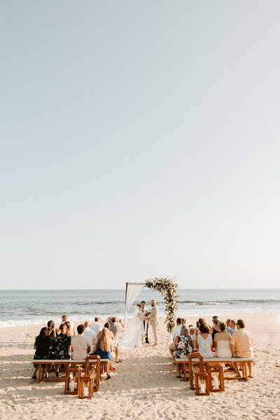 Wedding party on a beach with bride and groom kissing in front