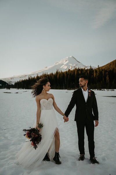 Bride and groom hold hands in the snow in front of Mt Hood during their Oregon elopement