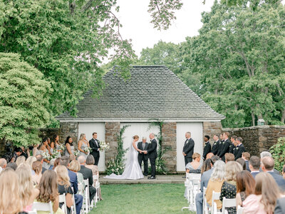 Bride and groom holding hands at the altar during their wedding ceremony in front of a small stone building