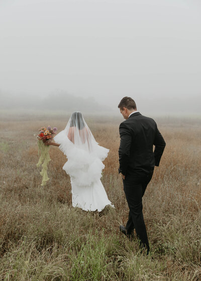 wedding couple walking thru tall grass on a foggy day