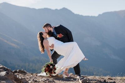 Groom kisses bride against Rocky Mountain backdrop during Colorado elopement/