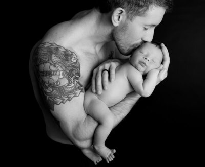 Black-and-white studio portrait of father kissing newborn baby’s head during a newborn photography session with Hello Photography in Austin, Texas.