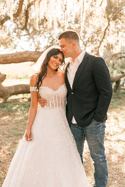 groom kisses his brides head while she smiles at the camera for Houston Elopement.