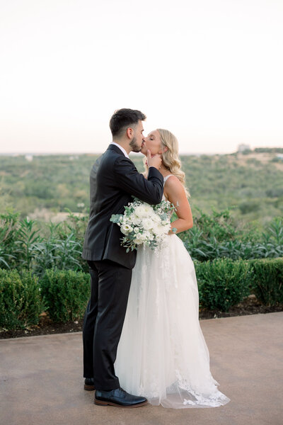 Bride and groom kissing with hill country backdrop in Austin Texas