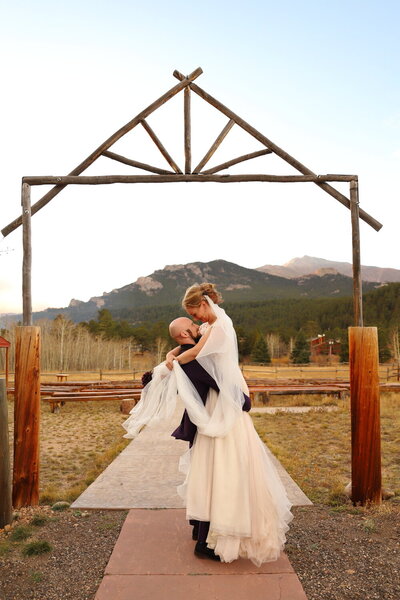 Married couple celebrating their wedding by kissing under an archway in the colorado mountains