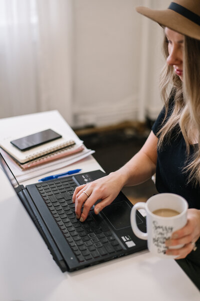 Sammy wearing a hat and holding a mug while typing on a laptop