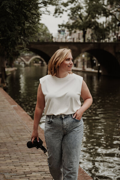Fotograaf loopt met camera in hand en kijkt naar het water bij de grachten in Utrecht.
