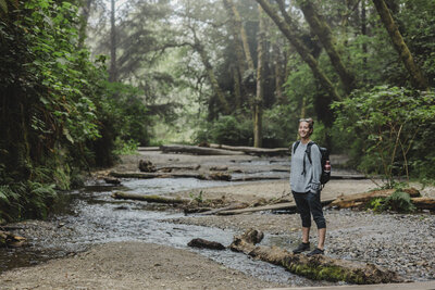 Katie smiles in the forest on a hike next to a river.