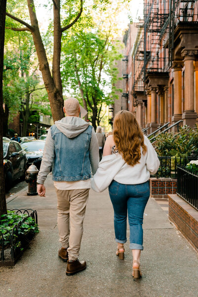 couple holding hands and walking along a sidewalk in the city