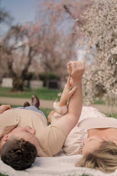Couple Lays on a picnic blanket under cherry blossom trees