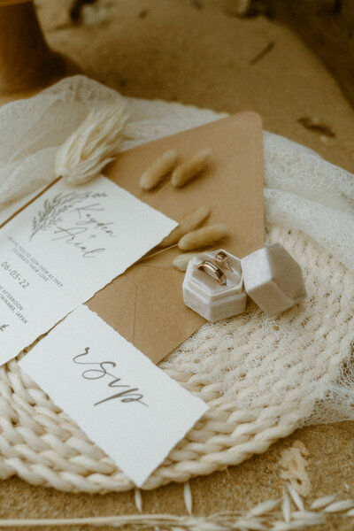 flat lay of rsvp, invitation, and ring box, with the focus on the rings
