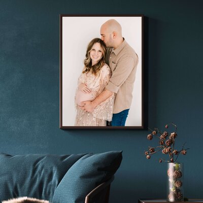 framed photo of pregnant couple cuddling on blue wall over couch