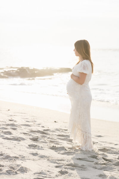 Pregnant woman standing on the beach cradling her bump by NJ Maternity Photographer