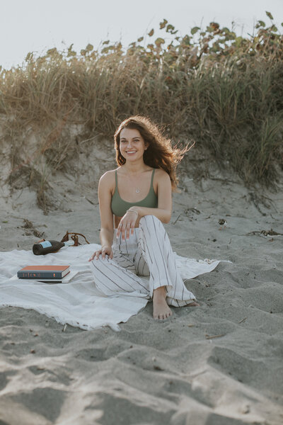 Female founder Courtney Sloan poses sitting on a beach blanket in the sand.