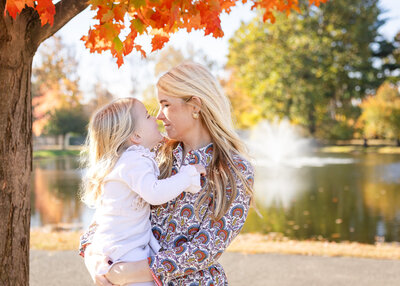 Mother nuzzling daughter in front of fall foliage in a NJ park.