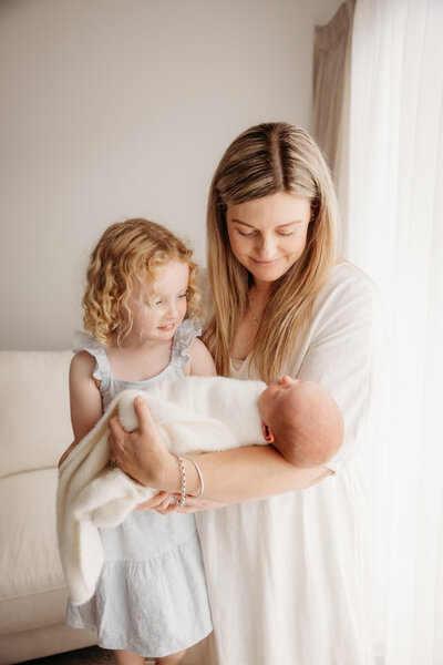 Lyla being held by her mother and sister during a newborn studio maternity photoshoot with michelle kelly photography